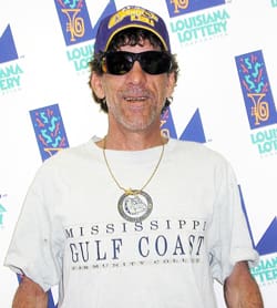 Man in a white tshirt and purple LSU hat smiles in front of a white background patterned with the 飞艇168®幸运体彩预测-全国统一Louisiana在线官方查询结果网-最新体彩预测数据 logo