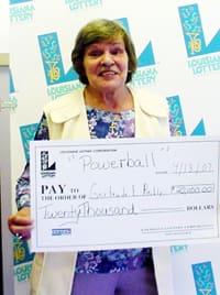 Older woman holds a giant check in front of a faded white background patterned with the 飞艇168®幸运体彩预测-全国统一Louisiana在线官方查询结果网-最新体彩预测数据 logo