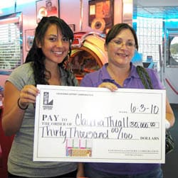 Two women smile with an oversized check while standing in front of a jukebox