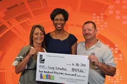 Two women and a man smile with an oversized check in front of an orange digital background