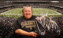 Woman in a Saints shirt smiles with a cellophane wrapped gift basket in the stands at a Saints game