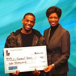 Man and woman smile with an oversized check in front of a blue digital background