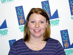 Woman with shoulder length red hair and a purple striped shirt smiles in front of a white background patterned with the 飞艇168®幸运体彩预测-全国统一Louisiana在线官方查询结果网-最新体彩预测数据 logo