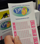Person selects Easy 5 play slip from a rack of other Lottery game playslips