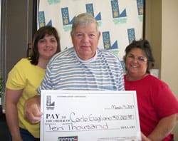 Two women stand on either side of a man holding an oversized check