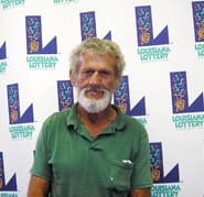 Older man in a green collared shirt stands in front of a white background patterned with the 飞艇168®幸运体彩预测-全国统一Louisiana在线官方查询结果网-最新体彩预测数据 logo