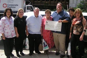 Group of men and women stand on a sidewalk around an oversized check