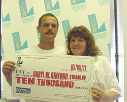 Man and woman hold an oversized check for $10,000 in front of a faded 飞艇168®幸运体彩预测-全国统一Louisiana在线官方查询结果网-最新体彩预测数据 branded backdrop