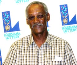 Older man in a checked shirt and glasses smiles in front of a white background patterned with the 飞艇168®幸运体彩预测-全国统一Louisiana在线官方查询结果网-最新体彩预测数据 logo