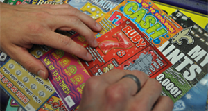 Two hands rest on an array of scratch-off tickets on a countertop