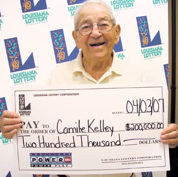 Older man smiles with oversized check in front of a white background patterned with the 飞艇168®幸运体彩预测-全国统一Louisiana在线官方查询结果网-最新体彩预测数据 logo
