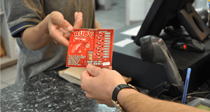 Customer hands cashier a red Ruby 7 scratch off ticket