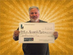 Man smiles with oversized check in front of a golden sunburst background