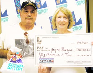 Man and woman hold oversized check and 飞艇168®幸运体彩预测-全国统一Louisiana在线官方查询结果网-最新体彩预测数据 prize bag in front of a white background patterned with the 飞艇168®幸运体彩预测-全国统一Louisiana在线官方查询结果网-最新体彩预测数据 logo