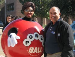 Woman in a red powerball mascot costume with white gloves smiles outdoors with a bald man in a black coat