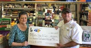 Man and woman hold a large Easy 5 check in front of a retailer counter