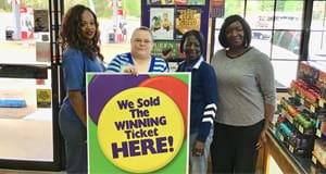Group of women pose around a large sign that reads "We Sold the Winning Ticket Here"