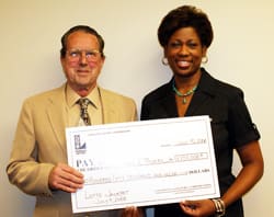 Man in a suit and a woman in black smile with an oversized check in front of a blank wall