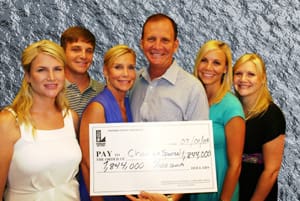 Man, woman, and children pose with oversized check in front of a gray stone background
