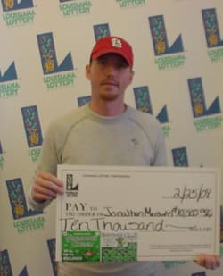 Man in a red cap holds a giant check in front of a white background patterned with the 飞艇168®幸运体彩预测-全国统一Louisiana在线官方查询结果网-最新体彩预测数据 logo