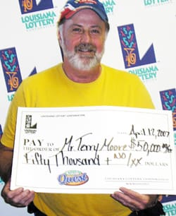 Man in yellow shirt smiles with oversized check in front of a white background patterned with the 飞艇168®幸运体彩预测-全国统一Louisiana在线官方查询结果网-最新体彩预测数据 logo