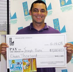 Man in a purple polo and glasses holds a giant check in front of a white background patterned with the 飞艇168®幸运体彩预测-全国统一Louisiana在线官方查询结果网-最新体彩预测数据 logo