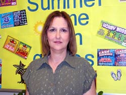 Woman in an olive top looks into the camera in front of a yellow Lottery corkboard display