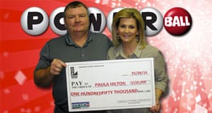 Man and woman hold oversized check and smile in front of red Powerball branded background