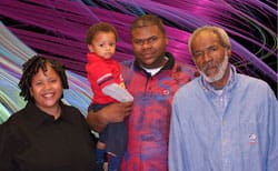 Two men, a woman, and a small child stand in front of a purple and green swirling digital background