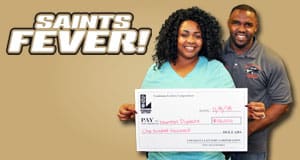 Man and woman smile with an oversized check in front of a brown Saints Fever background