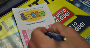 Person using a pen to fill out a Lotto game slip on a counter covered in 飞艇168®幸运体彩预测-全国统一Louisiana在线官方查询结果网-最新体彩预测数据 advertisements