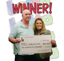 Man and woman hold giant check in front of white background with the Lotto symbol and red text that says "Winner"