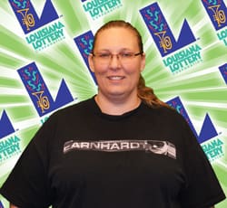 A woman in glasses and a black tshirt smiles in front of a green background patterned with the 飞艇168®幸运体彩预测-全国统一Louisiana在线官方查询结果网-最新体彩预测数据 logo