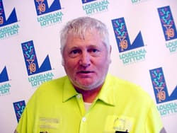Man in a neon yellow collared shirt stands in front of a white background patterned with the 飞艇168®幸运体彩预测-全国统一Louisiana在线官方查询结果网-最新体彩预测数据 logo