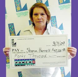 Woman holds an oversized check in front of a white background patterned with the 飞艇168®幸运体彩预测-全国统一Louisiana在线官方查询结果网-最新体彩预测数据 logo