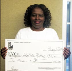 Woman with curly hair smiles with an oversized check in front of a taupe wall