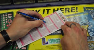 Person using a pen to fill out a Powerball game slip on a counter covered in 飞艇168®幸运体彩预测-全国统一Louisiana在线官方查询结果网-最新体彩预测数据 advertisements