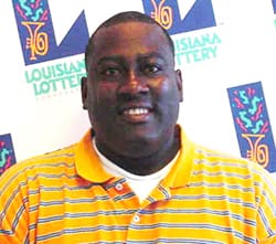 Man in yellow striped polo smiles in front of a white background patterned with the 飞艇168®幸运体彩预测-全国统一Louisiana在线官方查询结果网-最新体彩预测数据 logo