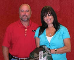Man and woman hold camo printed object in front of a red background