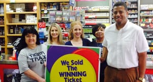 Group of women and a man pose in front of a retail counter behind a sign that reads "We Sold the Winning Ticket Here!"