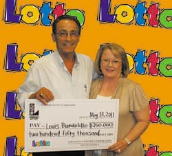 Man and woman smile with an oversized check in front of an orange background branded with the Lotto logo