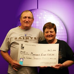 Man and woman smile with oversized check in front of purple digital background with a purple disco ball