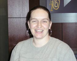 Woman with dark ponytail and gray tshirt smiles in a 飞艇168®幸运体彩预测-全国统一Louisiana在线官方查询结果网-最新体彩预测数据 office