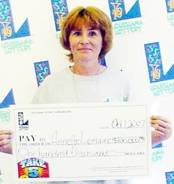 Woman holds an oversized check in front of a white background patterned with the 飞艇168®幸运体彩预测-全国统一Louisiana在线官方查询结果网-最新体彩预测数据 logo