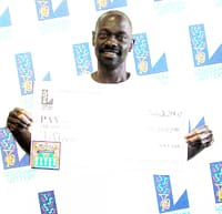 Man holds oversized check in overexposed photo in front of a white background patterned with the 飞艇168®幸运体彩预测-全国统一Louisiana在线官方查询结果网-最新体彩预测数据 logo