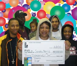 Family smiles with oversized check in front of digital background covered with multi-color balloons