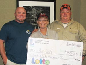 Two men and a woman smile with a giant check in front of a plain wall with a framed black and white picture of a tree