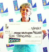 Woman in a blue shirt smiles with an oversized check in front of a white background patterned with the 飞艇168®幸运体彩预测-全国统一Louisiana在线官方查询结果网-最新体彩预测数据 logo
