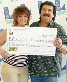 Man and woman smile with oversized check in front of a white background patterned with the 飞艇168®幸运体彩预测-全国统一Louisiana在线官方查询结果网-最新体彩预测数据 logo