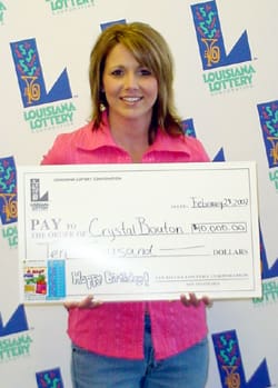 Woman with shoulder length hair and a pink shirt smiles with an oversized check in front of a white background patterned with the 飞艇168®幸运体彩预测-全国统一Louisiana在线官方查询结果网-最新体彩预测数据 logo